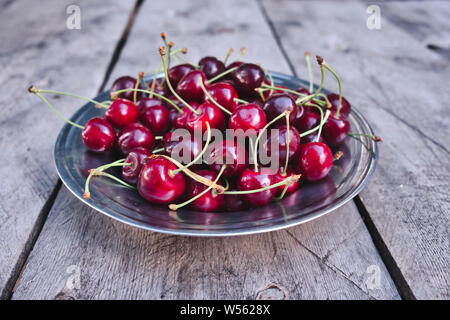 Kirsche, rote reife Kirschen in Platte und auf dem hölzernen Tisch Stockfoto