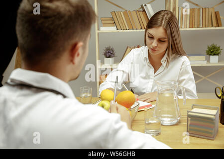 Die junge Frau, die ein Arzt für eine Ernährung Empfehlungen. Männliche Ernährungssachversta5ndiger bilden eine gesunde Diät Plan bis zum Patienten. Konzept der gesunden Lebensweise und Ernährung, Medizin und Behandlung. Stockfoto