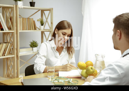 Die junge Frau, die ein Arzt für eine Ernährung Empfehlungen. Männliche Ernährungssachversta5ndiger bilden eine gesunde Diät Plan bis zum Patienten. Konzept der gesunden Lebensweise und Ernährung, Medizin und Behandlung. Stockfoto