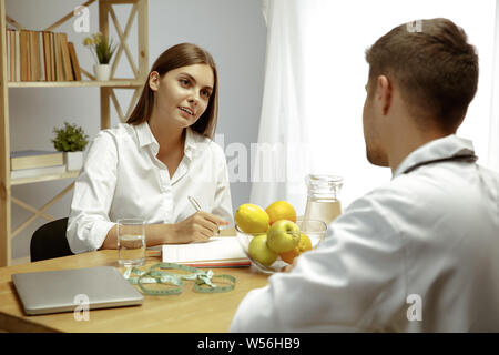 Die junge Frau, die ein Arzt für eine Ernährung Empfehlungen. Männliche Ernährungssachversta5ndiger bilden eine gesunde Diät Plan bis zum Patienten. Konzept der gesunden Lebensweise und Ernährung, Medizin und Behandlung. Stockfoto