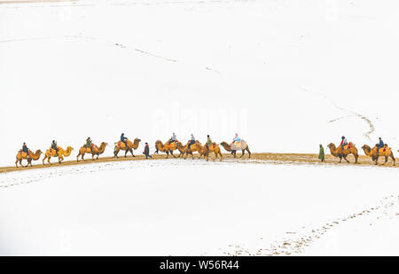 Touristen fahren Kamele in der Verschneiten Wüste Gobi im Crescent Moon Lake (Yueyaquan) und der singenden Sand Bergen malerischen Ort während der Chine Stockfoto