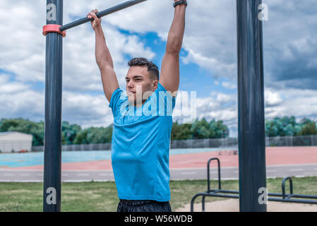 Jungen Kerl, man sports Sportler, im Sommer in der Stadt am Sportplatz, holt auf Bar, Workout Fitness, Workout gesunder Lebensstil. Sportswear, Stärke Stockfoto