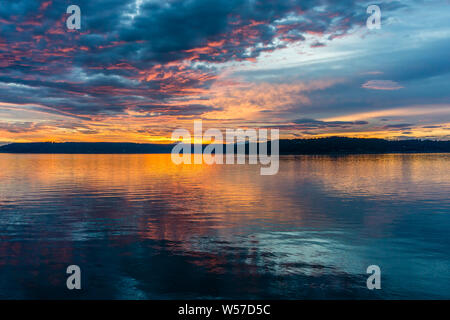 Die Wolken hängen am Himmel, wie die Sonne hinter den Olympic Mountains im Armaturenbrett, Washington. Stockfoto