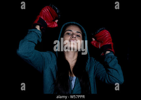 Porträt der jungen Frau Ausübung Boxen in der Turnhalle mit roten Handschuhe auf schwarzem Hintergrund Stockfoto