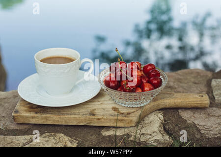 Kirschen und Tasse Kaffee auf schneidebrett an der Wand über dem Fluss Stockfoto