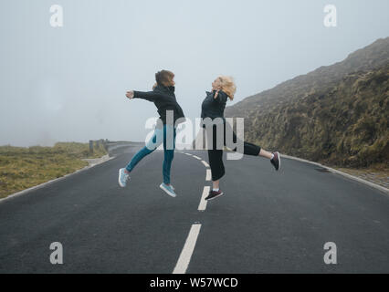 Zwei junge Frauen, springen auf einer Straße mit Nebel Stockfoto