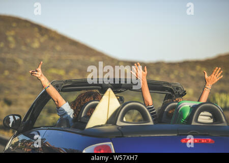 Von hinten ein paar euphorischen Frauen in einem Cabrio gesehen, Verdrehen, winken Zwei lockiges Mädchen im Urlaub, Spaß im Auto, glücklich lachend Stockfoto