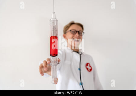 Nahaufnahme einer großen Spritze Junge selbst Identität als Medic amüsiert sadistisches Lachen. Junge Kind spielen als eine verrückte Arzt Spaß mit Blut. Stockfoto