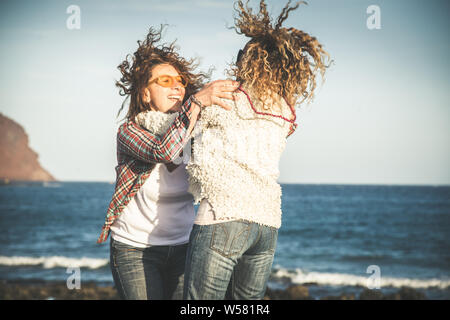 Freundschaft, Sommerurlaub, Freiheit, Glück Personen Konzept - zwei glückliche Frauen mittleren alter Freunde, die Sie umarmen sich, Tanzen springen Strand. Full- Stockfoto