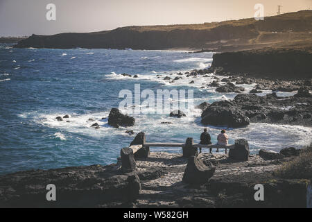 Zwei ältere Menschen, Frauen, sitzen auf einer Bank am Ufer im Sommer. Mit Blick auf das Meer vom Sandstrand entfernt. Sie denken, Erinnerungen, Stockfoto