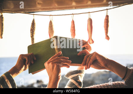 In der Nähe von Mutter und Sohn Händen ein Buch lesen zusammen im Wohnmobil im Licht des Sonnenuntergangs liegen. Konzept der Familie und Zeit zu teilen. Mutter ein Stockfoto