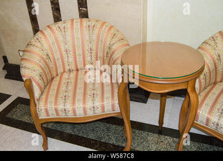 Klassisch elegante Sessel und einem kleinen Holztisch mit gebogenen Beine, in Vintage Retro Stil, Marmorboden und Wänden im Wohnzimmer eines Luxus Stockfoto