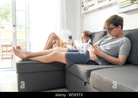 Zwei Jungs spielen mit Smartphones auf dem Sofa. Brüder mit Handy. Drahtlose Technologie ermöglicht überall in Verbindung zu bleiben. Konzept Bild Stockfoto