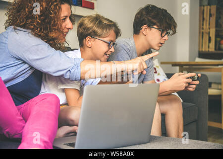 Familie sitzt auf sofà zu Hause mit der Spielkonsole. Mutter lächelnd mit zwei jungen Brüder spielen video game. Spiele online mit Freunden. Werden Stockfoto