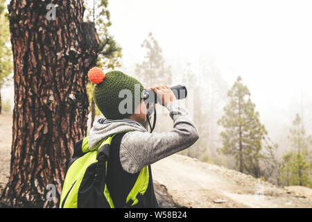 Kind von hinten gesehen mit fluoreszierenden Rucksack sieht Fernglas erkunden Natur des wilden Bergwald. Family Adventure Discovery im Freien leben. Y Stockfoto