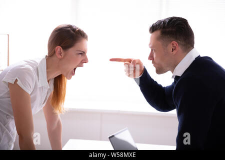 Seitenansicht des Geschäftsmannes Zeigefinger an Geschäftsfrau beim Kämpfen im Büro Stockfoto