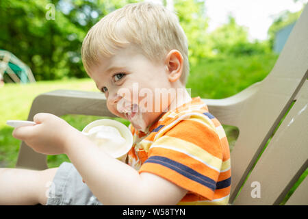 Gerne blonde Toddler boy isst Eis draußen, während es tropft auf Kinn Stockfoto