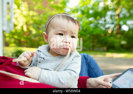 Baby Mädchen in der Mutter Schoß kaut auf shirt Strings, während die rechten suchen Stockfoto