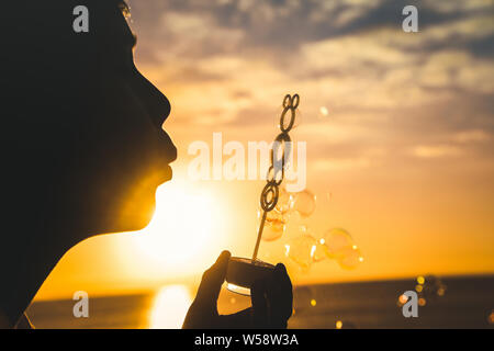 Junge blonde Junge bläst eine lange Reihe von Blasen in ein Feld; niedliche Kind vor dem Meer jagen Seife kochen, schönes Kind spielen im Freien in einem schönen Stockfoto