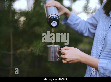Reisende Mädchen gießt Kaffee aus der Thermoskanne Schale, im Freien. Junge Frau trinkt Kaffee in der Tasse. Thema Reisen. Frau gießen ein heißes Getränk in Becher aus der Thermoskanne. Gi Stockfoto