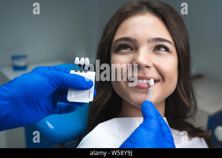 Zahnarzt in Blau medizinische Handschuhe, die Probe, die von Zahnschmelz Maßstab zu glückliche Frau Patienten Zähne bis rechten Farbton für die Zähne zu bleichen Stockfoto