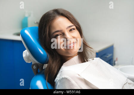 Glückliche junge schöne Frau zum Patienten, der auf zahnmedizinischen Stuhl unter der medizinischen Lampe in Klinik Stockfoto