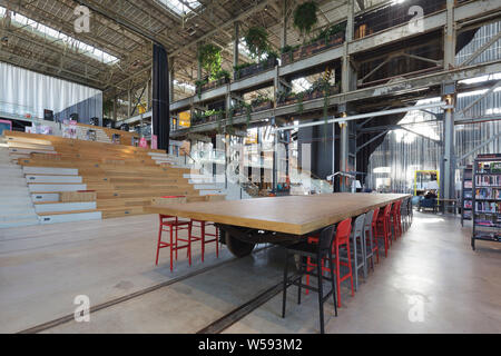 Grosse Treppe vom Erdgeschoss gesehen, mit Gemeinschafts-lesetisch im Vordergrund. Bibliotheek LocHal, Tilburg, Niederlande. Architekt: CIVIC Architekt Stockfoto