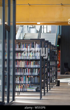 Regale mit massiven orange Stahlträger Overhead. Bibliotheek LocHal, Tilburg, Niederlande. Architekt: CIVIC Architekten/Braaksma & Roos Architekten Stockfoto