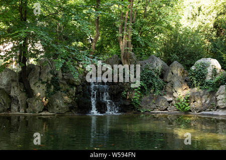 Ein Teich mit einem kleinen Wasserfall im Park (Liechtensteinpark) hinter dem Gartenpalais Liechtenstein in Wien, Österreich. Stockfoto