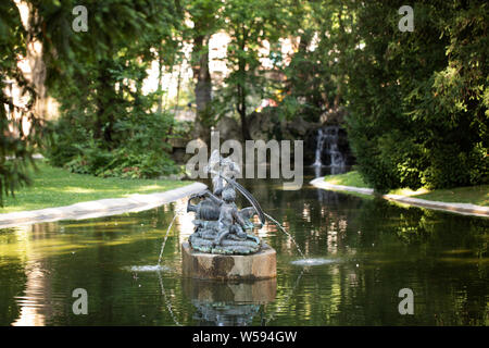 Ein Teich mit einer Brunnenstatue und einem kleinen Wasserfall im Park (Liechtensteinpark) hinter dem Gartenpalais Liechtenstein in Wien, Österreich. Stockfoto