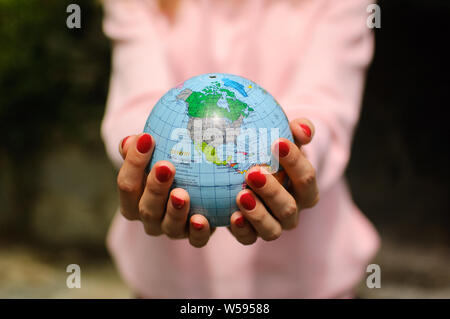 Die Mädchen in ein rosa Pullover mit roten Maniküre hält eine kleine Kugel mit geografische Namen im Ukrainischen kyrillischen Buchstaben. Nordamerika ist sichtbar Stockfoto