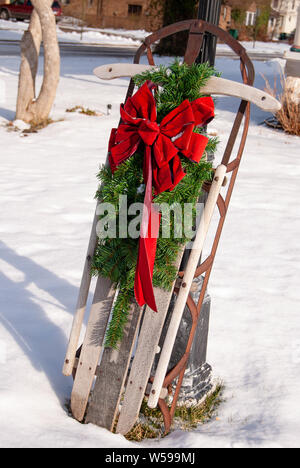 Weihnachten kiefer Ast mit leuchtend roten Schleife auf retro Holz Schlitten im Schnee Stockfoto