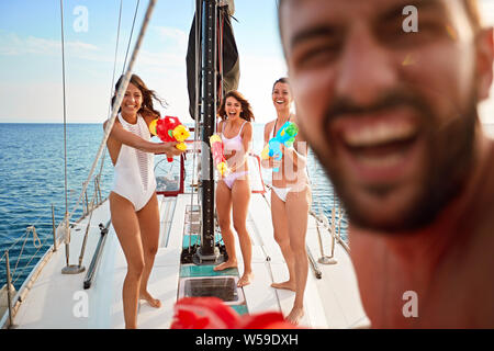 Glückliche Menschen spielen auf Segelboot mit Wasserpistolen auf Urlaub. Stockfoto