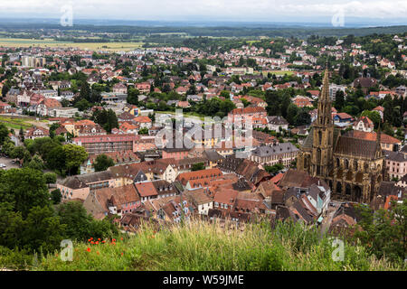 Mit Blick auf die malerischen elsässischen Stadt Thann, Frankreich einschließlich der mittelalterlichen St. Theobald Kirche an einem bewölkten Tag Französisch. Stockfoto