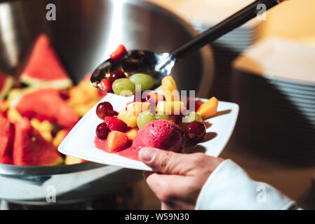 Person dient, Obstsalat und Eis Stockfoto