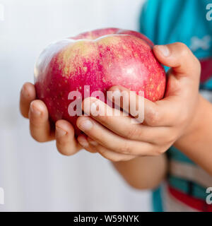 Der Junge hält einen großen, roten Apfel. Ein Kind mit einer saftigen Frucht. Polnische Äpfel. Gesundes Frühstück. Stockfoto