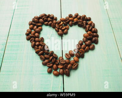 Herzform aus Kaffeebohnen auf Holzoberfläche gefertigt. Stockfoto