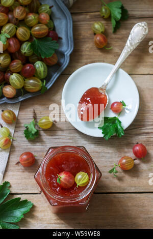 Stachelbeermarmelade im Glas und Stachelbeerbeeren auf einem Holztisch. Rustikaler Stil. Stockfoto