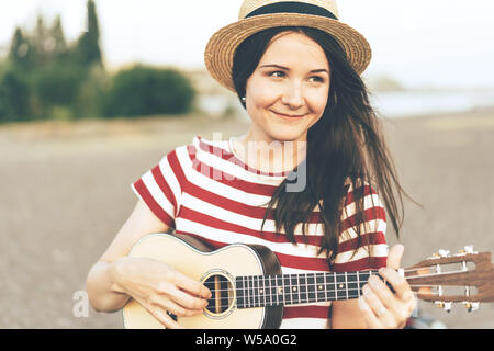 Brunette Mädchen in einem strohhut Spielen der Ukulele. Gypsy Hawaiian Lifestyle. Stockfoto