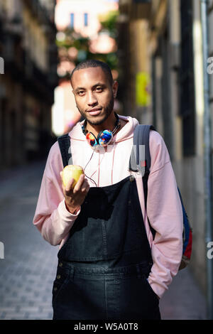 Junge schwarze Mann ißt einen Apfel auf der Straße. Stockfoto