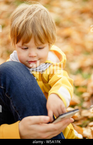 Konzept: Familie, Kinder. Glückliches Kind, baby boy Lachen und Spielen mit der Mutter Smartphone im Herbst auf der Wanderung in der Natur draußen im Park