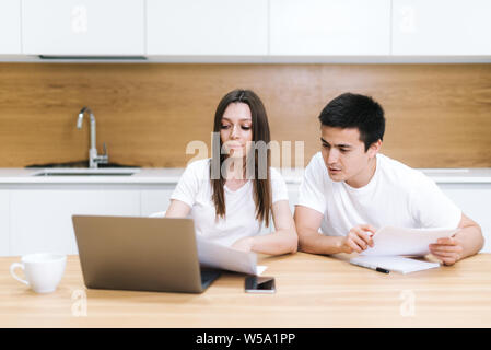 Junges Paar die Verwaltung der Finanzen, ihre Bankkonten Überprüfung mit Laptop Computer in moderne, helle Küche. Frau und Mann Papiere zusammen tun, Stockfoto