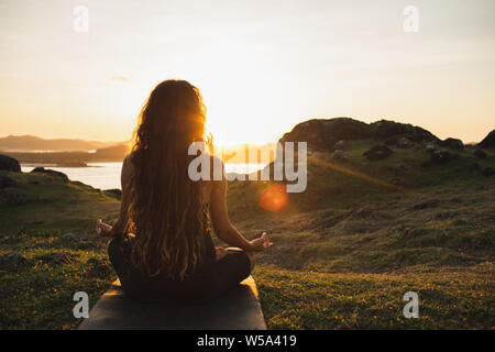 Meditation frau yoga allein bei Sonnenaufgang in den Bergen. Ansicht von hinten. Reisen Lifestyle geistige Entspannung Konzept. Harmonie mit der Natur. Stockfoto