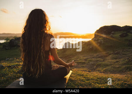 Meditation frau yoga allein bei Sonnenaufgang in den Bergen. Ansicht von hinten. Reisen Lifestyle geistige Entspannung Konzept. Harmonie mit der Natur. Stockfoto