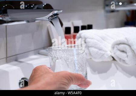 Wasserhahn mit fließendem Wasser, Hand und trinken Glas Stockfoto