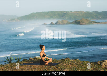 Frau Yoga und Sitzen im Lotussitz im Freien mit herrlichem Blick auf das Meer. Gesundheit und Wohlbefinden Konzept. Natur Hintergrund. Stockfoto