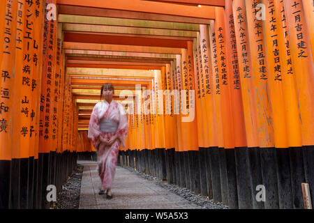 Eine junge Frau geht unter den torii Gates im Fushimi Inari Schrein in Kyoto, Japan. Der Kopf Heiligtum des Gottes Inari in Kyoto, den Fushim entfernt Stockfoto