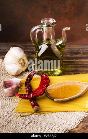 Immer noch leben. Rohe Spaghetti mit Knoblauch Nelken, einige getrocknete Peperoni- und Olivenöl auf dem rauen Holz- Tabelle Stockfoto