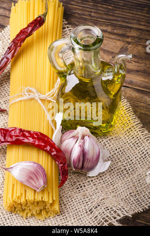 Immer noch leben. Rohe Spaghetti mit Knoblauch Nelken, einige getrocknete Peperoni- und Olivenöl auf dem rauen Holz- Tabelle Stockfoto