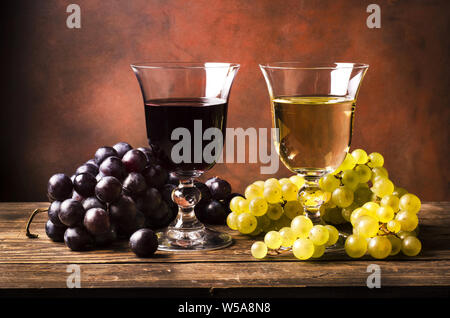 Auf rustikalen Holztisch Gläser Weiß- und Rotwein, mit gemischten Trauben Stockfoto